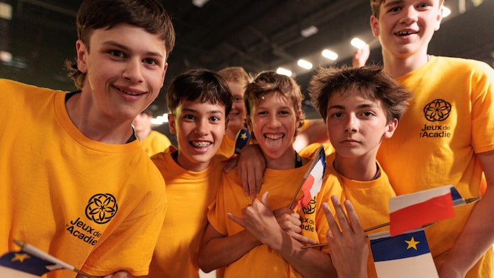 Des jeunes hommes souriant tenant des drapeaux de l'Acadie.