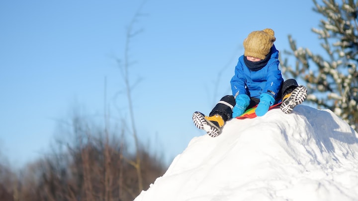 Un enfant au sommet d'un monticule de neige sur sa luge.