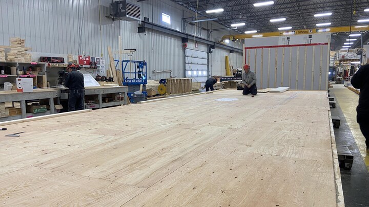 Un travailleur à l'oeuvre, à genoux sur un grand plancher de bois en usine.