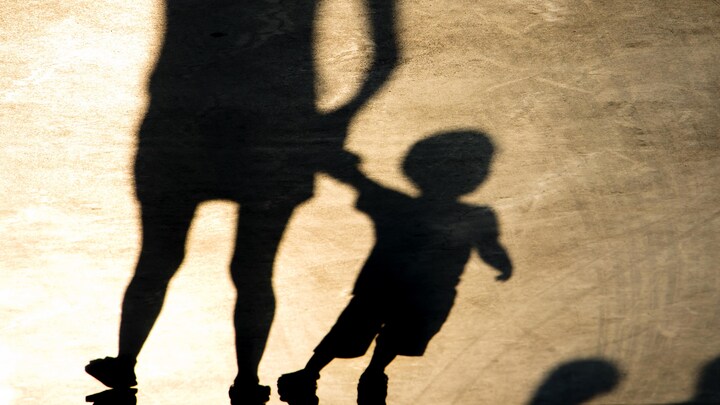 Les ombres d'une femme et d'un petit garçon qu'elle tient par la main apparaissent sur un sol en béton.