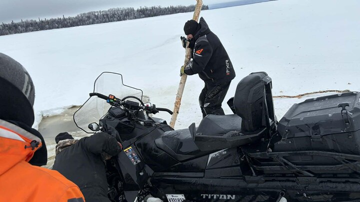 Trois personnes tentent de sortir le devant d'une motoneige de l'eau.