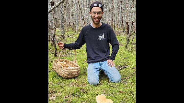 Olivier Brien est agenouillé sur le sol près d'un panier rempli de champignons.