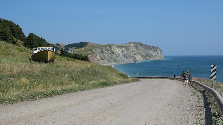 Une way   en gravier au bord de l'eau, avec des falaises au loin, sur l'archipel des Îles-de-la-Madeleine.
