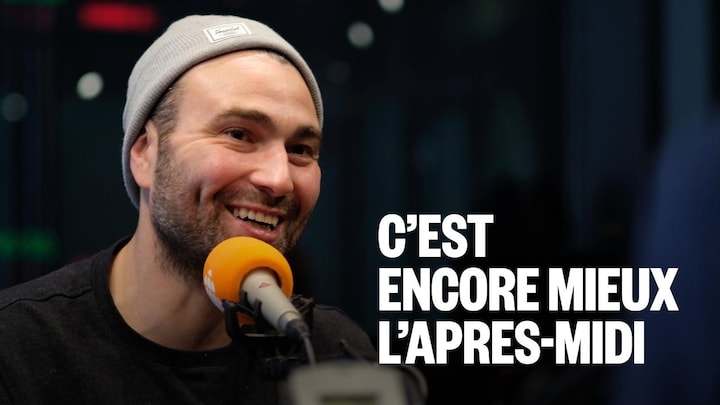Un homme avec une tuque sourit devant un micro dans un studio de radio.