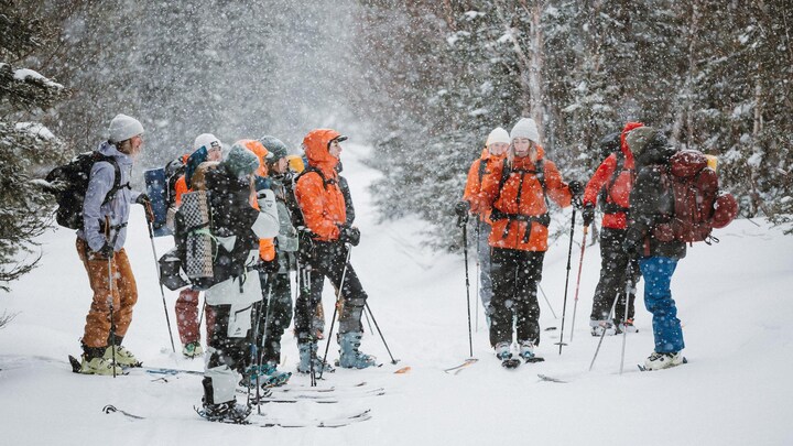 Une dizaine de femme en ski avec des sacs à dos au milieu d'un sentier sous la neige.