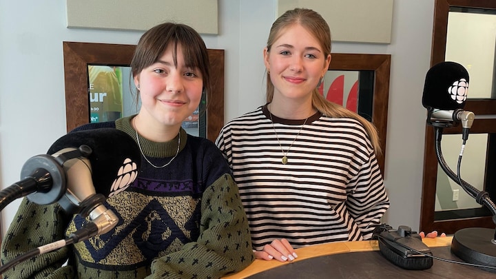 Félixe Rivest-Leclerc et Élizabeth L'Heureux sourient à la caméra en prenant la pose derrière un micro, dans un studio de Radio-Canada.
