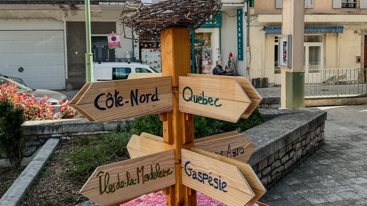 Un poteau en bois avec des flèches où sont inscrites les noms de régions du Québec.