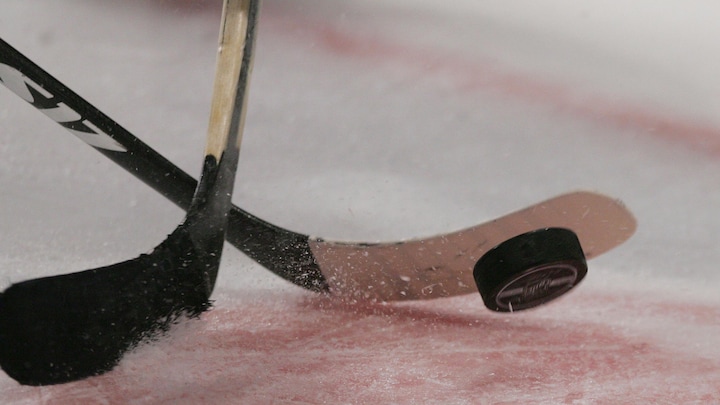 Deux bâtons de hockey et une rondelle, lors d'une mise au jeu.