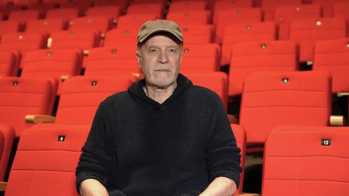 Une homme portant un chandail noir et une casque. Derrière lui, les sièges rouges d'une salle de spectacles.