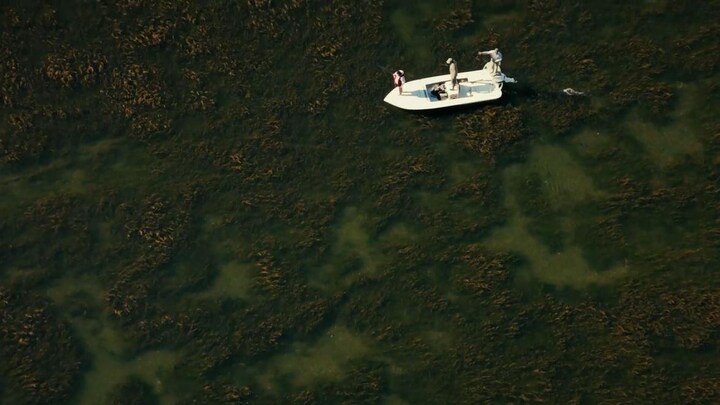 Un bateau de pêche avec trois personnes à son bord dans des eaux peu profondes.