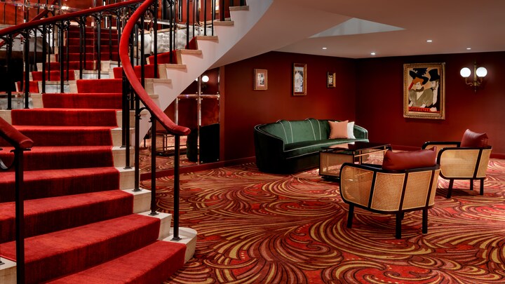 On peut voir des fauteuils avec une table haute et des affiches sur les murs ainsi qu'un tapis de couleur brune.