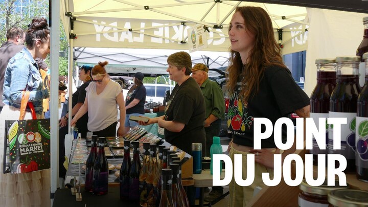 Une commerçante à son kiosque est entourée de bouteilles. Des clients en arrière-plan.