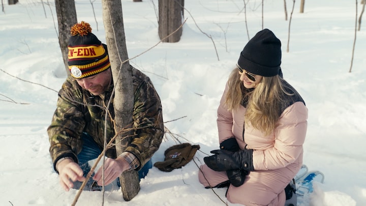 Un homme et une femme en train d'installer un collet en forêt, pendant l'hiver.