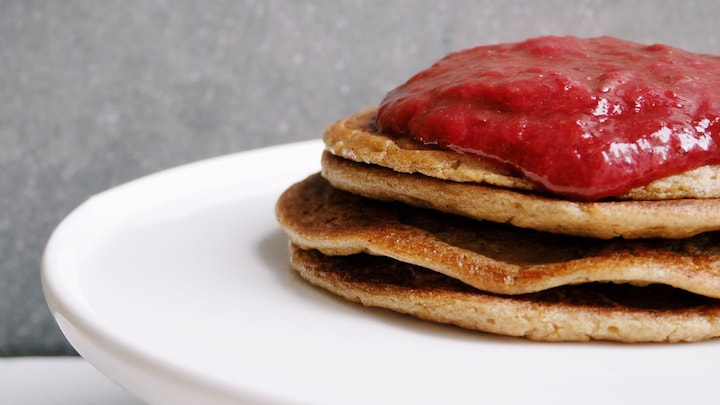 Quatre pancakes sur un plat de service servi avec de la compote.