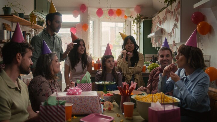 Un groupe de personnes réunies autour d'une table festive. Ils ont toutes et tous des chapeaux pointus et colorés sur la tête. 
