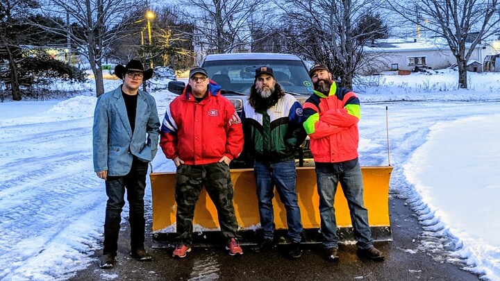 Quatre hommes devant une grande pelle de déneigement.