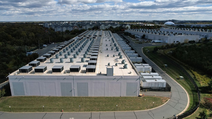Photo aérienne de larges bâtiments rectangulaires blancs, hauts de seulement quelques mètres, avec de petits stationnements presque inoccupés.
