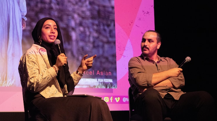 رجل وامرأة جالسان على كراسي على خشبة مسرح.