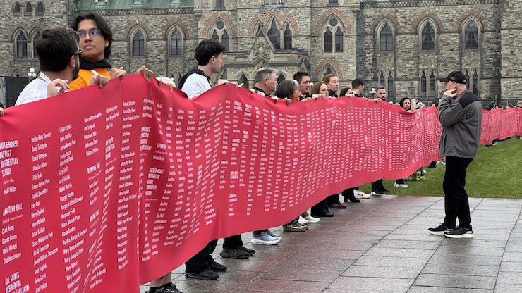 En los actos del Día de la Verdad y la Reconciliación este 30 de septiembre, varias personas sostienen una larga pancarta con los nombres de las víctimas de los internados para indígenas, frente al Parlamento, en Ottawa.