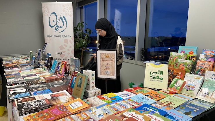 امرأة تقف أمام مجموعة كتب معروضة على طاولة.