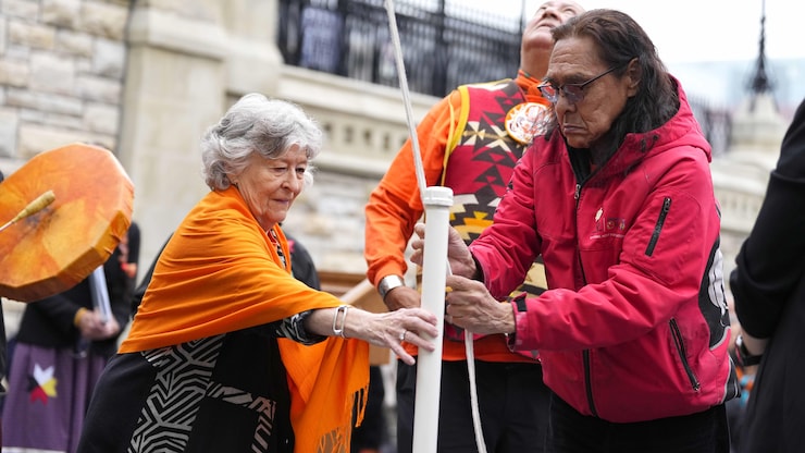 La gouverneure générale Louise Arbour aide à stabiliser un mât pendant que Bernard Andreason, survivant des pensionnats pour Autochtones, attache les cordes.