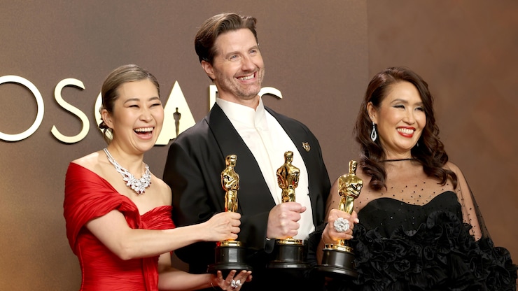 Les cinéastes et la productrice sont tout sourire sur scène avec leurs statuettes. 