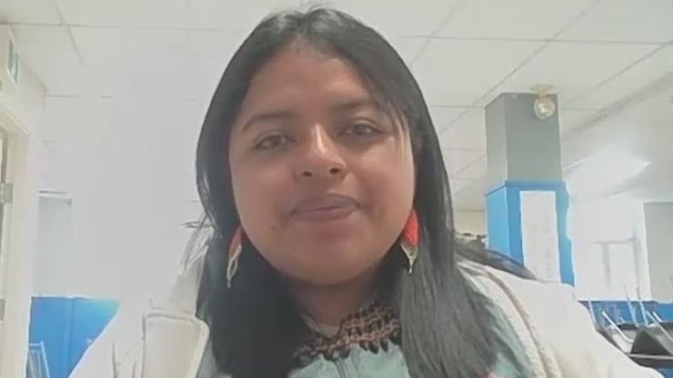 ES: Mujer joven de cabello oscuro con pendientes rojos y chaqueta blanca, posando en una oficina.
FR: Jeune femme brune avec des boucles d'oreilles rouges et une veste blanche dans un bureau.
EN: Young dark-haired woman wearing red earrings and a white jacket, looking at the camera indoors.