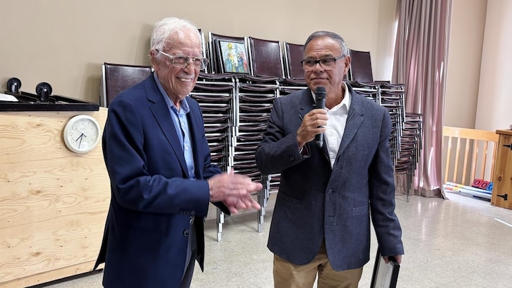 ES: Hombre con un diploma habla por micrófono mientras un hombre mayor aplaude feliz.
FR: Un homme avec un diplôme parle au micro pendant qu'un homme âgé applaudit.
EN: A man holding a certificate speaks into a mic while an older man claps happily.