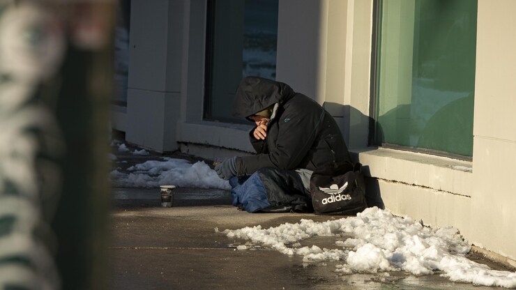 متشرد جالس على الرصيف في تورونتو وأمامه كوب يجمع فيه صدقات المارة.