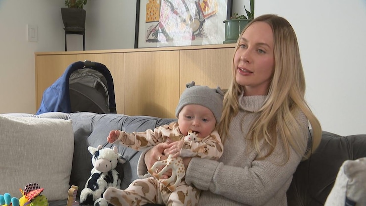 A woman sits on a sofa with a baby on her lap and a toy giraffe.