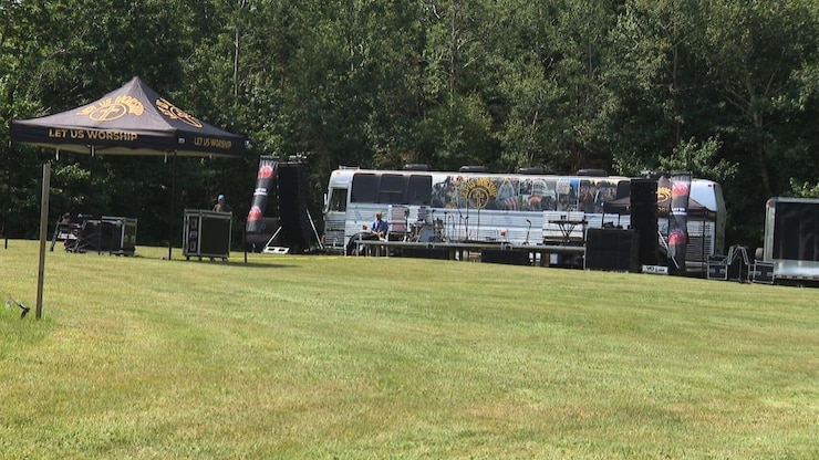A tour bus, a tent and trailers on a lawn next to a treeline.