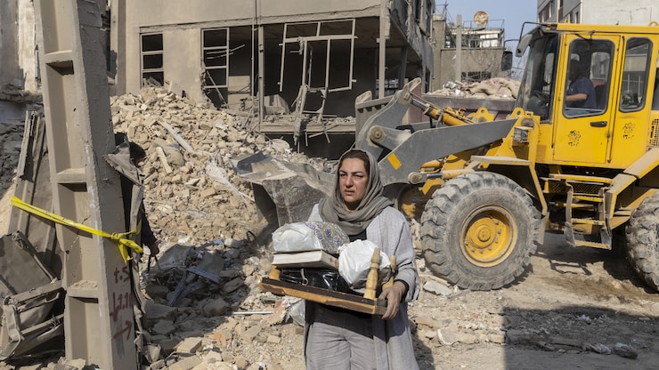 Une femme récupère des effets personnels le 14 mars 2026 sur le site de bâtiments, dont un commissariat de police, détruits lors d'une frappe aérienne il y a deux jours dans le quartier de Khani Abad à Téhéran, en Iran. 