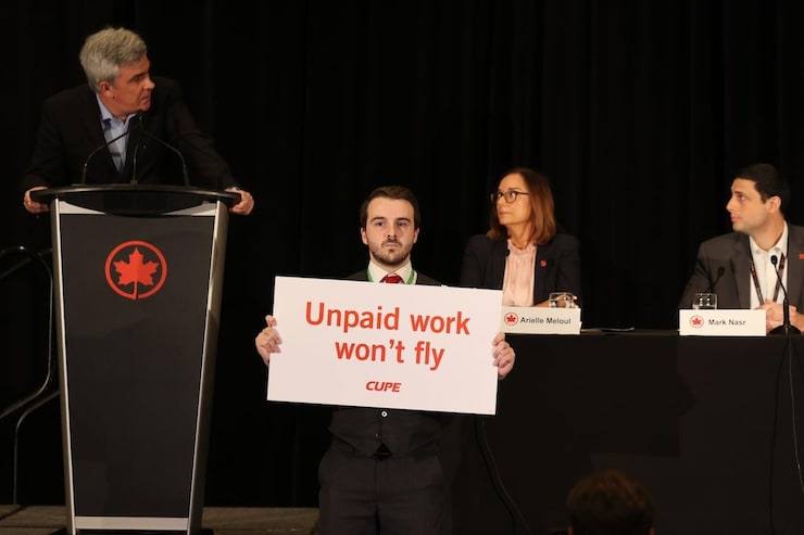 A flight attendant holds a sign saying 'Unpaid work won't fly' while three people hold a press conference.