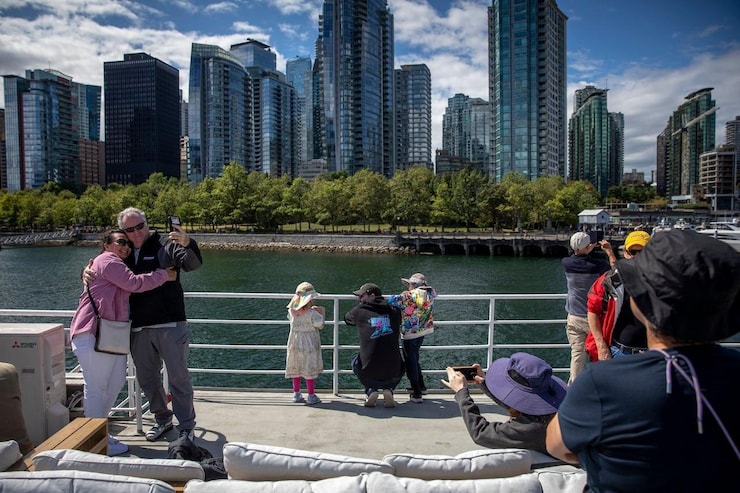 Tourists on a boat look at tall buildings in Vancouver.
