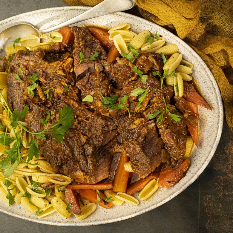Une assiette de bœuf braisé accompagné de pâtes courtes aux œufs.