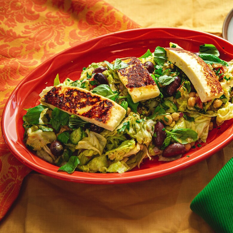 Une assiette de service remplie de salade méditerranéenne contenant des olives, de la laitue, des pois chiches et du fromage halloumi.