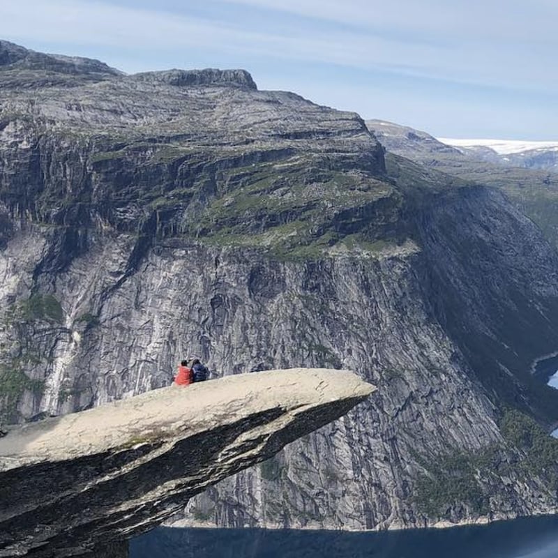Deux personnes sont assises sur un pic rocheux au-dessus d'une falaise à Trolltunga en Norvège.