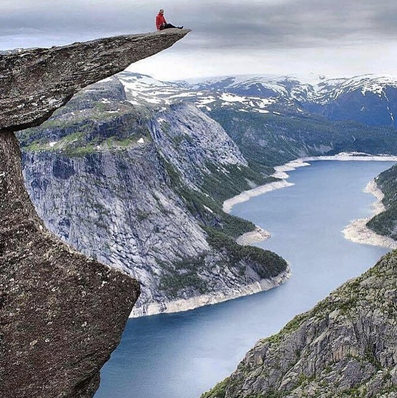 Une personne est assise au bout d'un pic rocheux au-dessus d'une falaise à Trolltunga en Norvège.