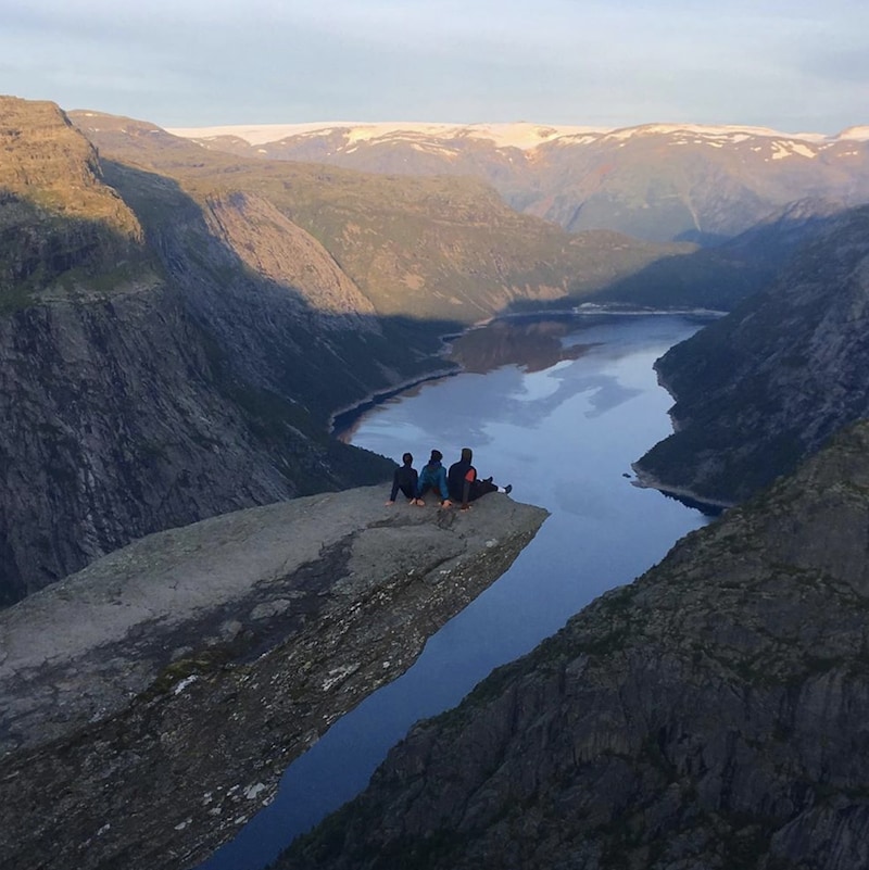 Trois personnes sont assises sur le bout d'un pic rocheux au-dessus d'une falaise à Trolltunga en Norvège.