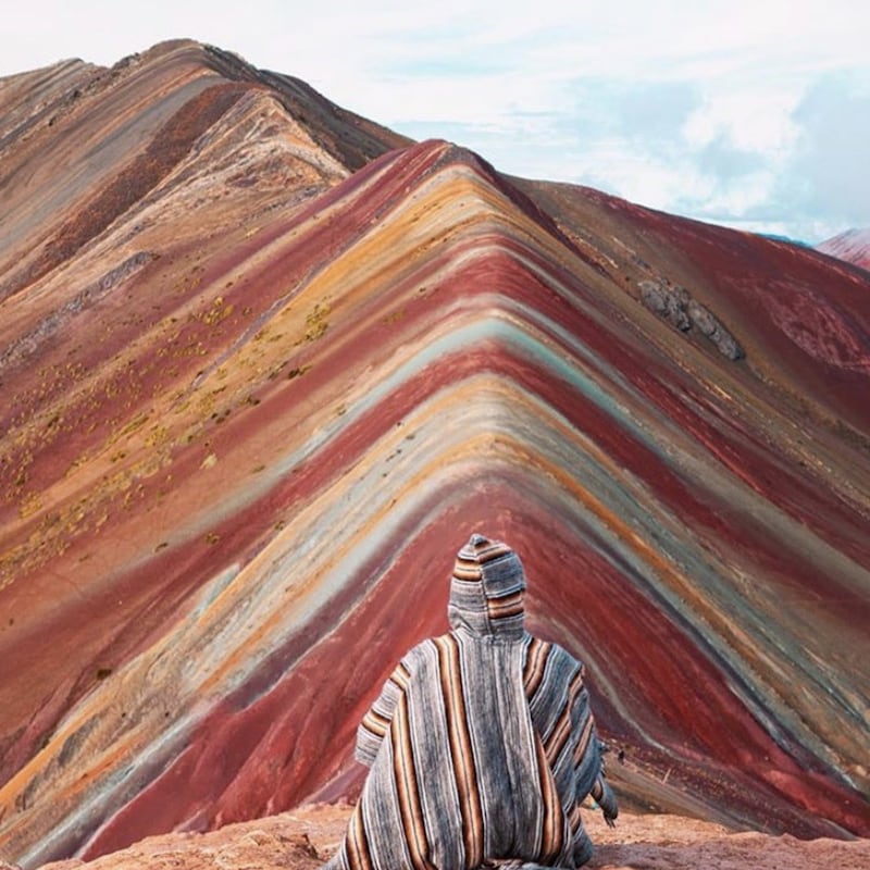 Une personne assise au sommet de la montagne Vinicunca, ou montagne aux sept couleurs, au Pérou