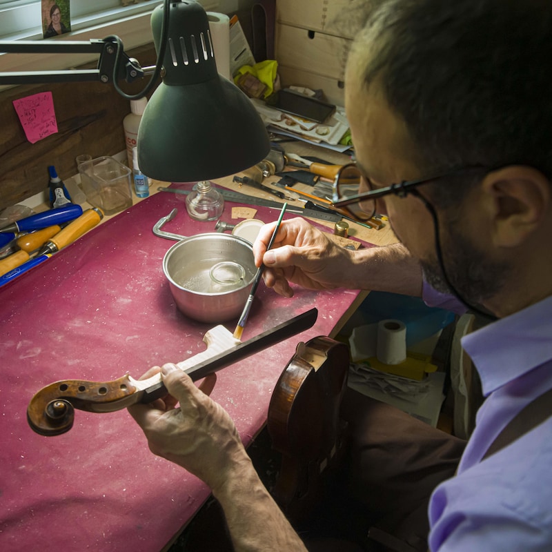 Le luthier applique de la colle sur le manche à l'aide d'un pinceau.