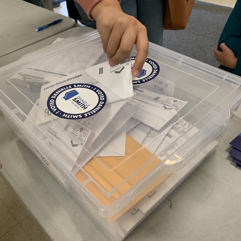 Une personne dépose un bulletin de vote dans une boîte de plastique transparent.