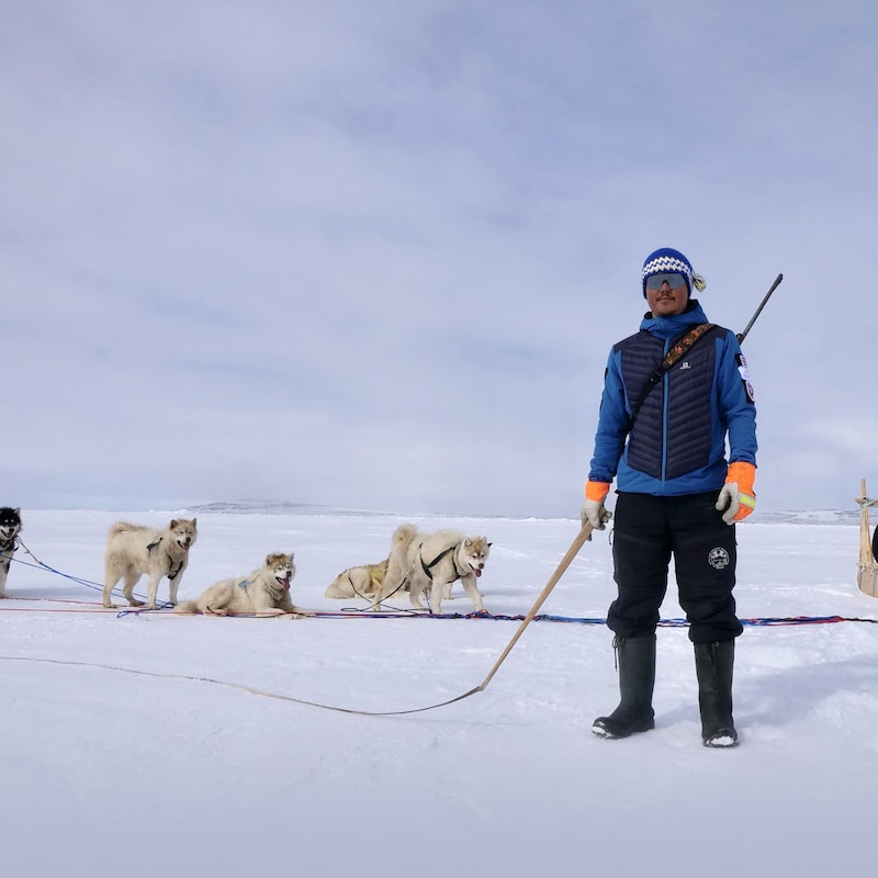 Devon Manik est debout sur la banquise, un fouet à la main devant son traîneau avec ses chiens, au mois de juin à Resolute Bay, dans le nord du Nunavut.