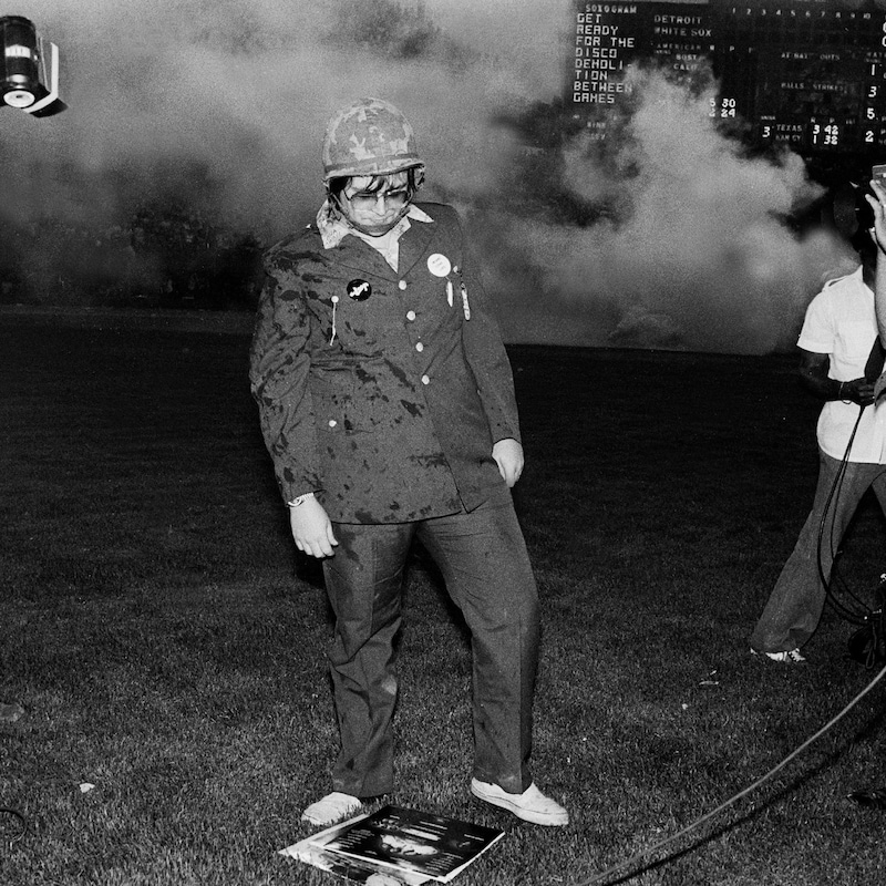 Steve Dahl jette un regard de dédain à des vinyles disco étalés sur la pelouse  du stade de baseball des White Sox de Chicago.