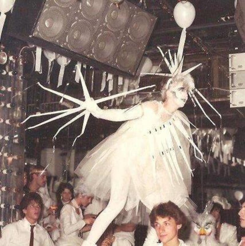 Une personne costumée en blanc danse sur une table dans une discothèque.