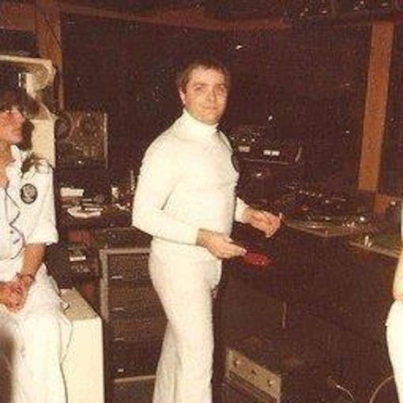 Tout vêtu de blanc, Robert Ouimet prend la pose dans la cabine où il mixe la musique.
