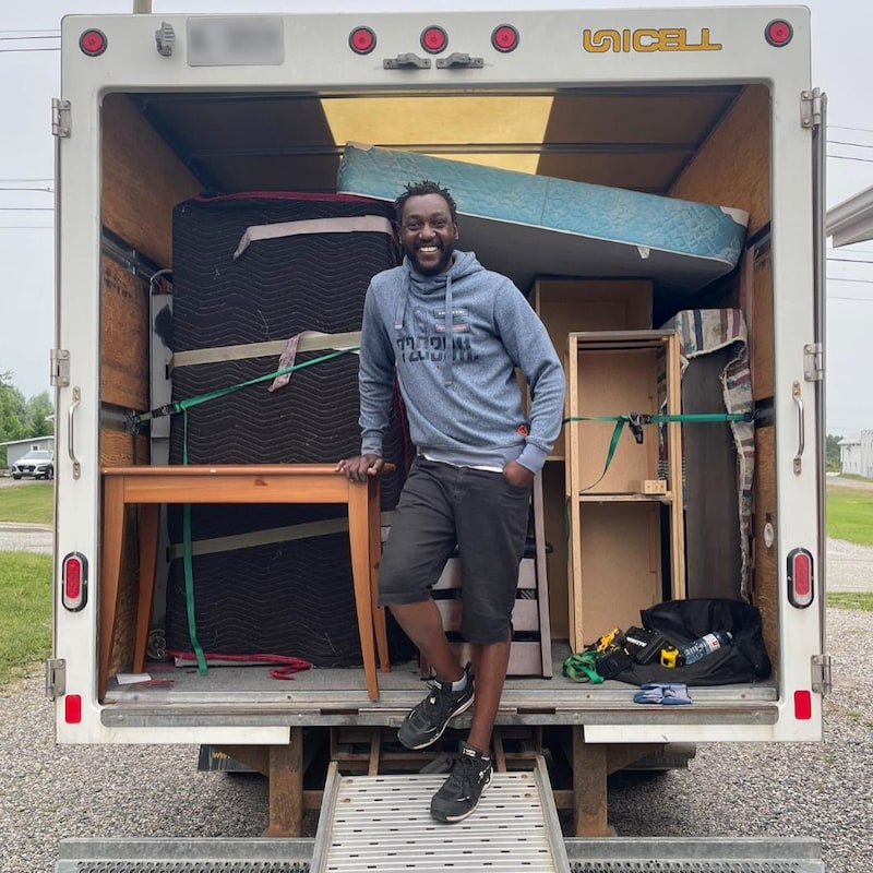 Stessy Ndongo Mombo sourit fièrement devant ses meubles attachés dans un camion de déménagement.