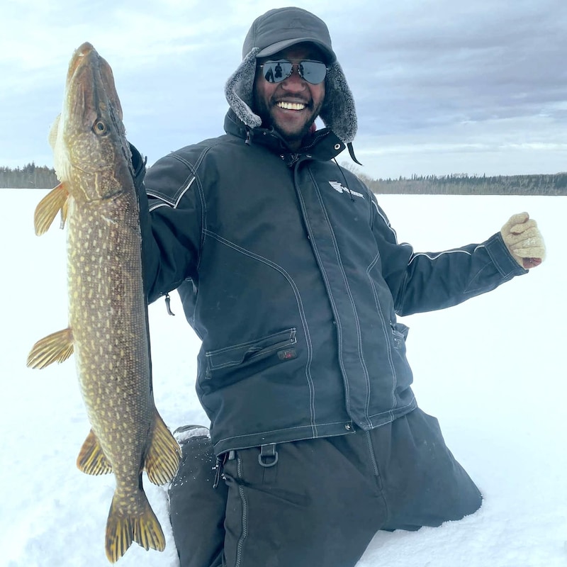 Stessy Ndongo Mombo tient fièrement un brochet dans une main sur un lac gelé en hiver.