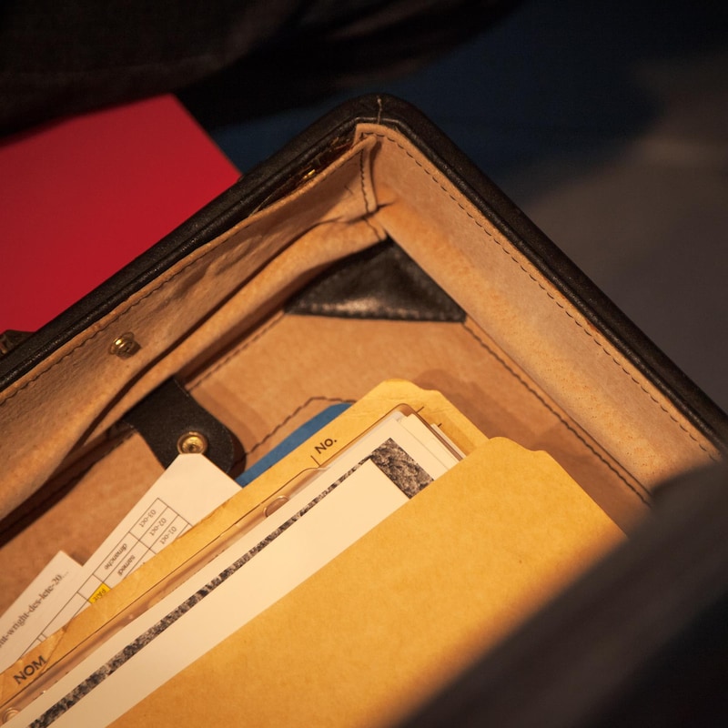 Une pile de documents sont placés dans une fiche en carton, dans une mallette entrouverte.