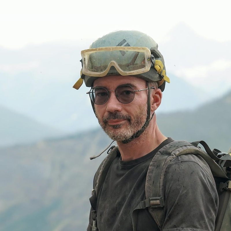 Jean-Bernard Caron avec un casque et des lunettes de protection, au sommet d'une montagne. 